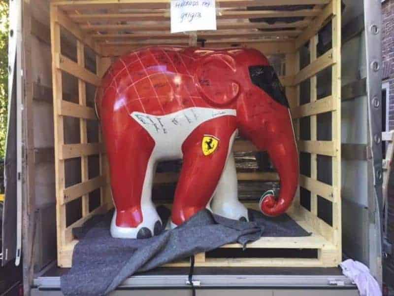 Éléphant Ferrari 3 Sztuczny słoń pomalowany w kolorach Ferrari, umieszczony w drewnianej skrzyni transportowej.