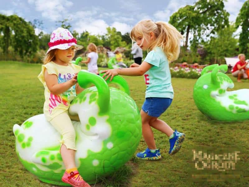 Figurines dans le parc d'attractions 1 Dzieci bawiące się na zielonym trawniku z kolorowymi, zielono-białymi, dużymi zabawkami w kształcie ślimaków.