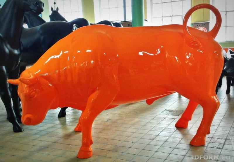 Pomarańczowa rzeźba byka znajdująca się w środku, na tle czarnych rzeźb koni