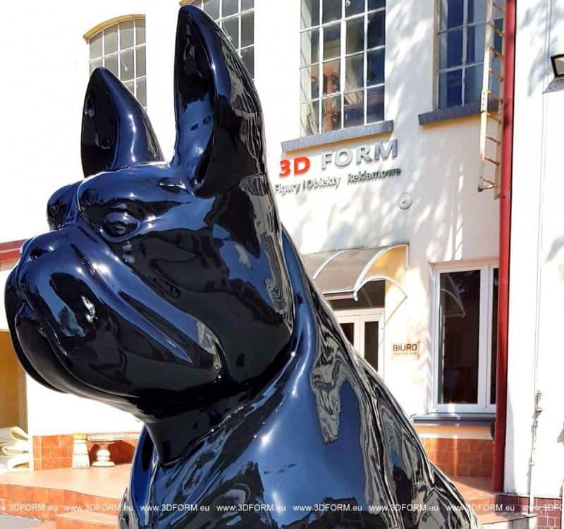 Czarna rzeźba psa przed budynkiem z napisem 