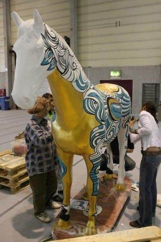 Grandes figures peintes par des enfants 3 Ludzie malujący dużą rzeźbę konia w budynku.