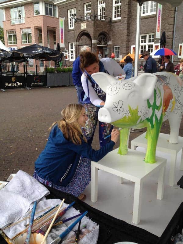 Grandes figures peintes par des enfants 1 Kobiety malują wielką rzeźbę krowy na zewnątrz budynku.