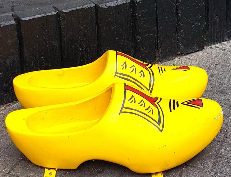 Grands Sabots 2 Żółte drewniaki z czerwono-czarnym wzorem, stojące na chodniku przy murze.