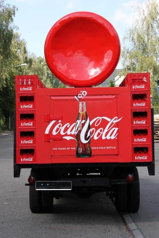 Camion publicitaire Coca-Cola 4 Tył czerwonej ciężarówki promującej Coca-Colę z dużą butelką i logo marki.