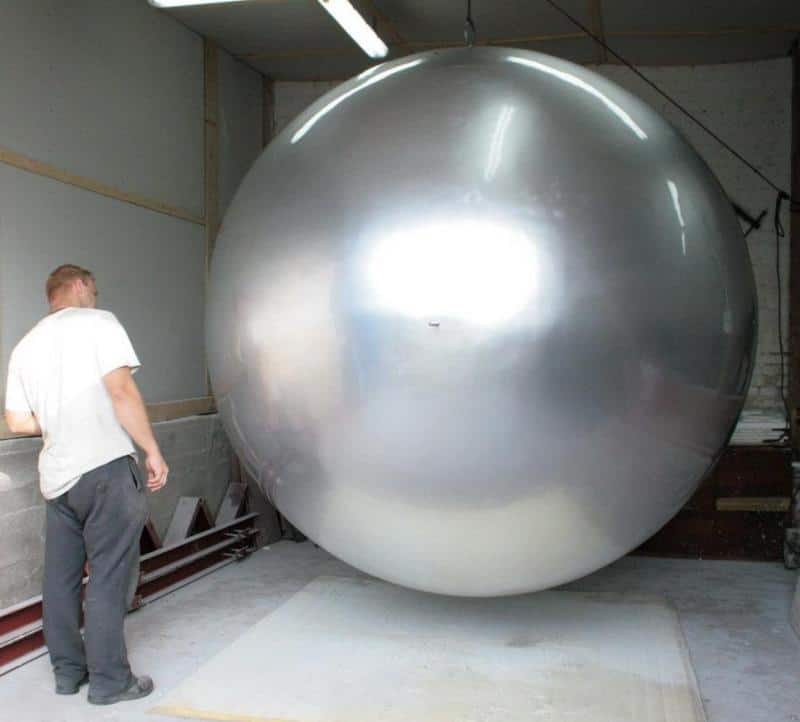 Grande Sphère dans l'Espace Urbain 4 Mężczyzna stojący obok ogromnej, srebrnej kuli w hangarze.