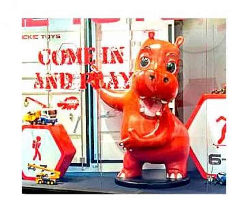 Hippopotame Publicitaire 2 Czerwona figurka hipopotama w witrynie sklepowej z napisem