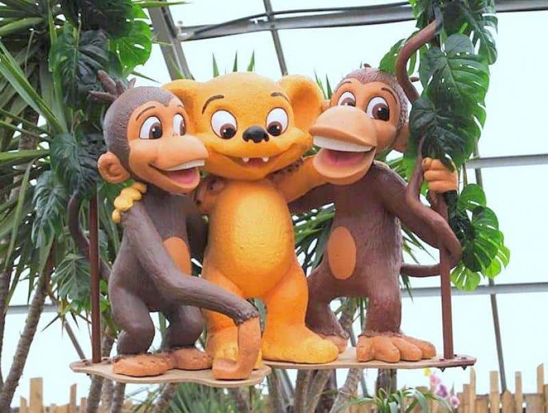 Figures pour parc d'attractions - Hugo Land 2 Trzy postacie kreskówkowe: dwa małpy i jeden stwór o pomarańczowej sierści, stoją razem na huśtawce w otoczeniu roślin.