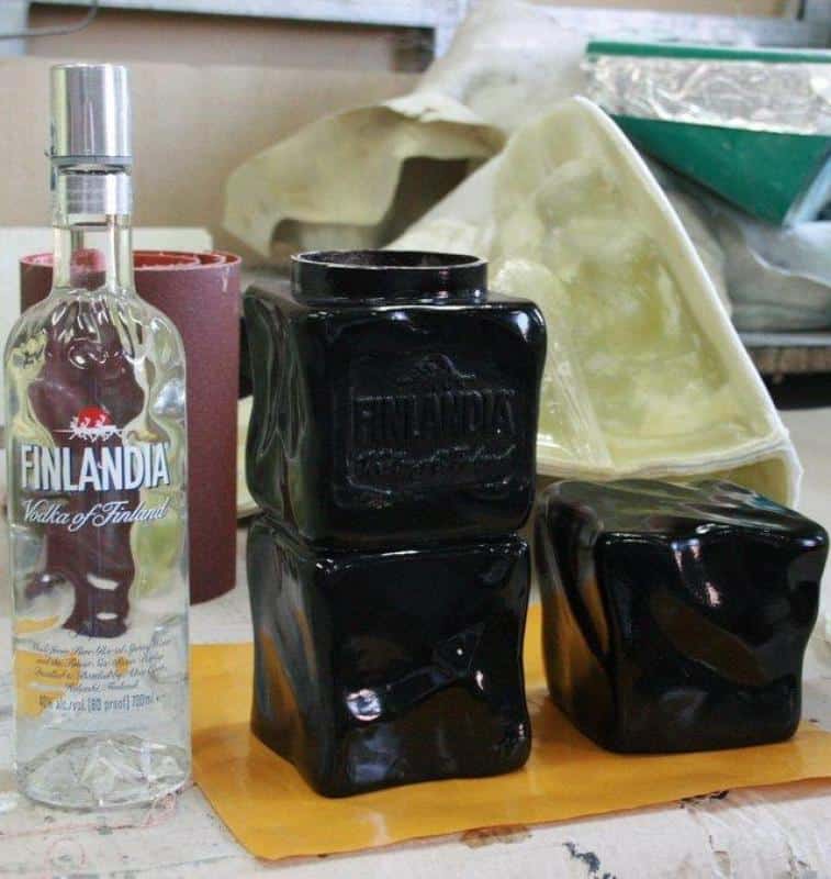 Emballage promotionnel Finlandia 2 Butelka Finlandia Vodka To/1750 ml oraz trzy czarne, zdeformowane butelki Finlandia umieszczone na stole roboczym.