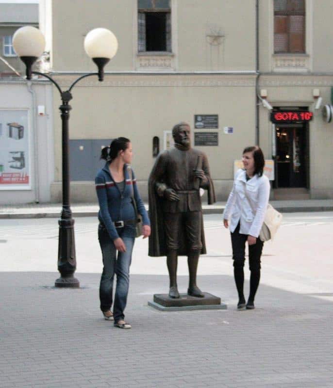 Monument - Kepler 4 Dwie kobiety obok rzeźby mężczyzny na chodniku w mieście.