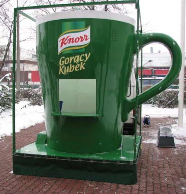 Publicité mobile - grande tasse KNORR 1 Zielona gigantyczna filiżanka Knorr Gorący Kubek na zewnątrz, zimowa sceneria w tle.