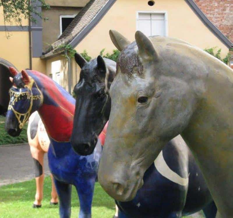 Trzy kolorowe rzeźby koni ustawione w ogrodzie przed domem.