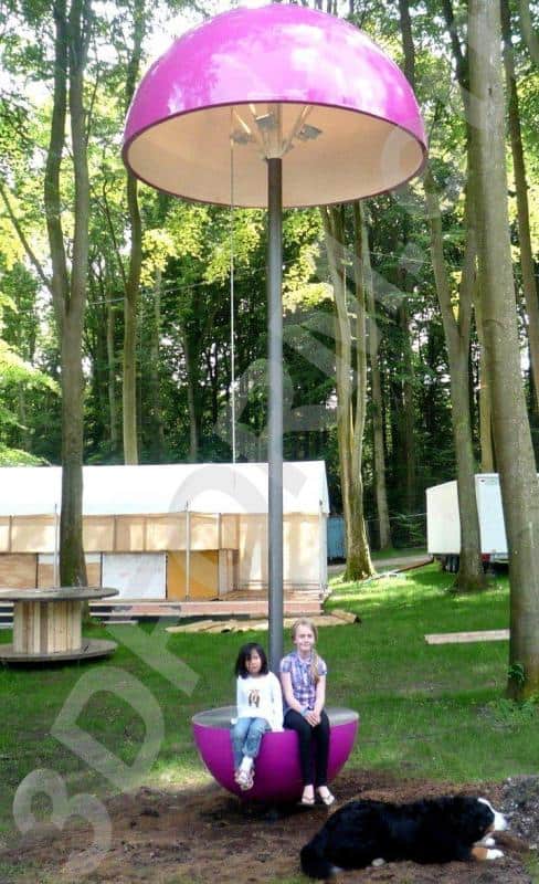 Lampes de festival 2 Dwoje dzieci siedzących na różowej huśtawce w kształcie grzyba w lesie, obok leży czarny pies.