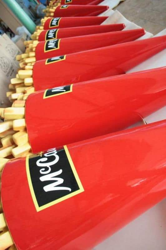 Frites publicitaires McCain 1 Czerwone pudełka na frytki z logo McCain ustawione w rzędzie na stole.