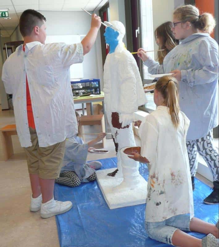 Sculptures de Mineurs 2 Dzieci malują stojącą rzeźbę człowieka w szkolnej sali.