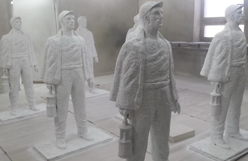 Sculptures de Mineurs 4 Posągi górników trzymających lampy górnicze ustawione w pomieszczeniu.