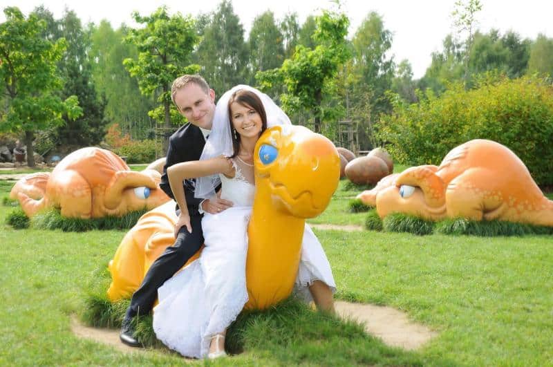 Para młoda siedząca na dużej, pomarańczowej figurce zwierzęcia w parku.