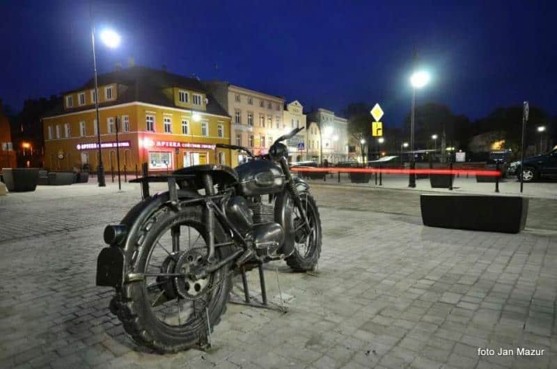 Moto Iconique - Monument à Żagań 4 Motocykl na placu miejskim nocą, w tle oświetlone kamienice.