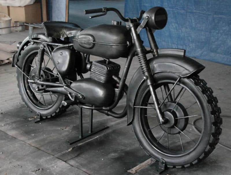 Moto Iconique - Monument à Żagań 1 Czarny, zabytkowy motocykl na tle niebieskiej ściany.