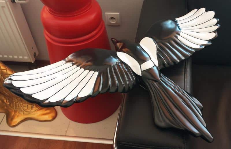 Czarna rzeźba ptaka z rozłożonymi skrzydłami leżąca na kanapie.