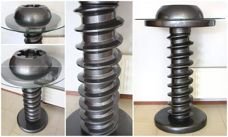 Stolik z podstawą wykonaną z dużej śruby stalowej, ze szklanym blatem.