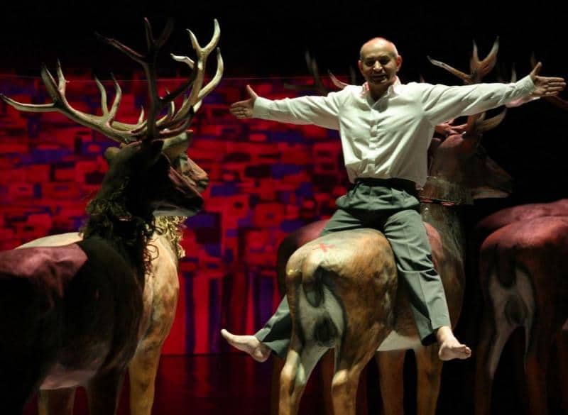 Éléments de scénographie pour le Théâtre Dramatique de la Ville Capitale de Varsovie 4 Mężczyzna siedzący na makiecie jelenia na scenie z czerwono-fioletowym tłem.