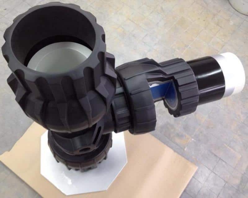 Té - Raccord de Tuyauterie 4 Czarny element mechaniczny o skomplikowanej budowie, z przegubem i uchwytem, na tle kartonowej powierzchni.