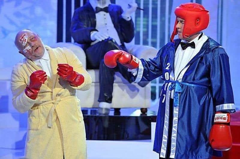 TVP2 - Éléments de Décor 2 Dwóch mężczyzn ubranych w stroje bokserskie i rękawice bokserskie podczas występu scenicznego, jeden w szlafroku, a drugi w niebieskim szlafroku bokserskim i kasku ochronnym.