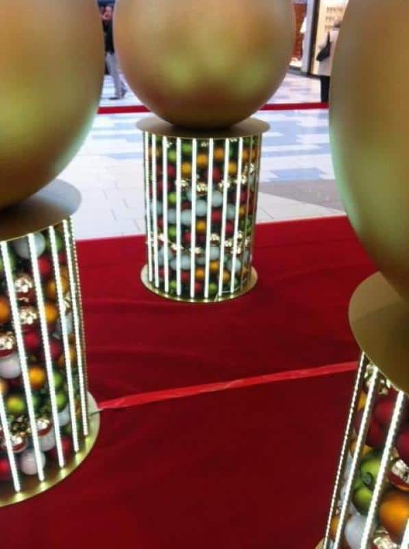 Boules de Noël éclairées 3 Duże złote kule na cylindrycznych stojakach w galerii handlowej.