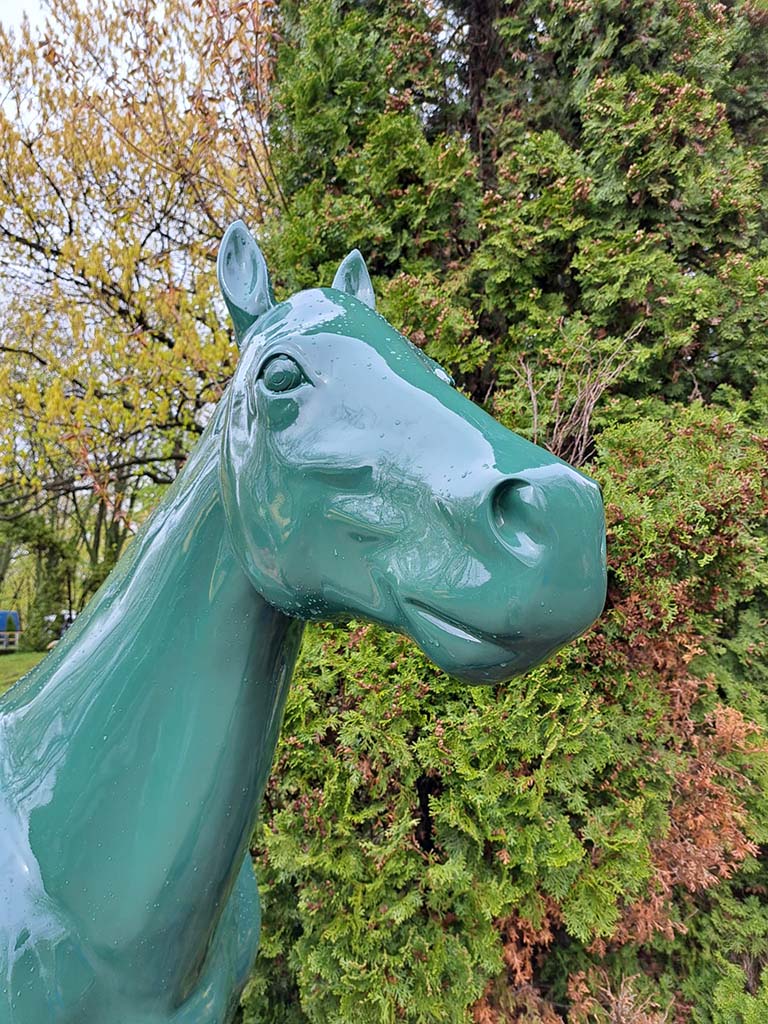 Zielona rzeźba konia na tle drzew.