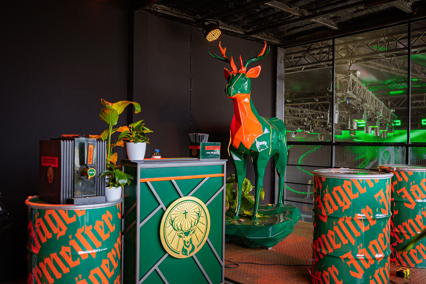 Kolorowy, geometryczny jeleń oraz elementy dekoracyjne marki Jägermeister w barze ozdobionym roślinami.