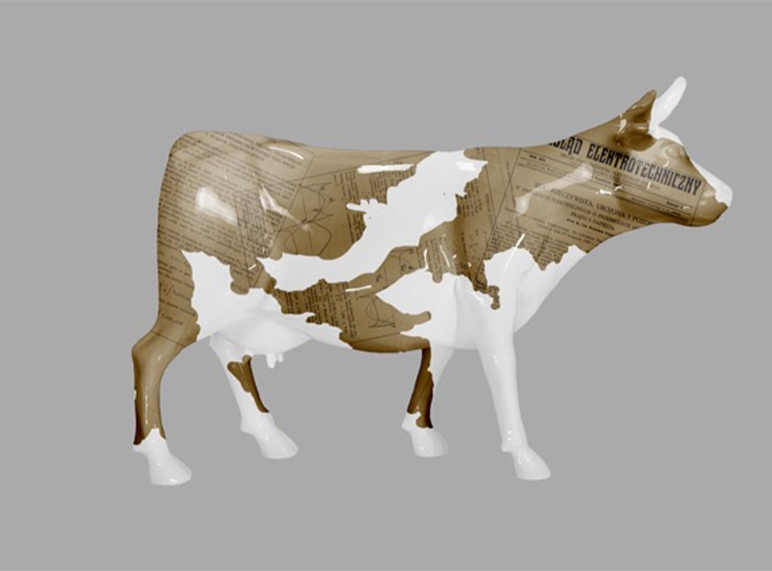 Model krowy o brązowo-białej skórze z nadrukiem starych dokumentów technicznych na brązowych fragmentach, na szarym tle
